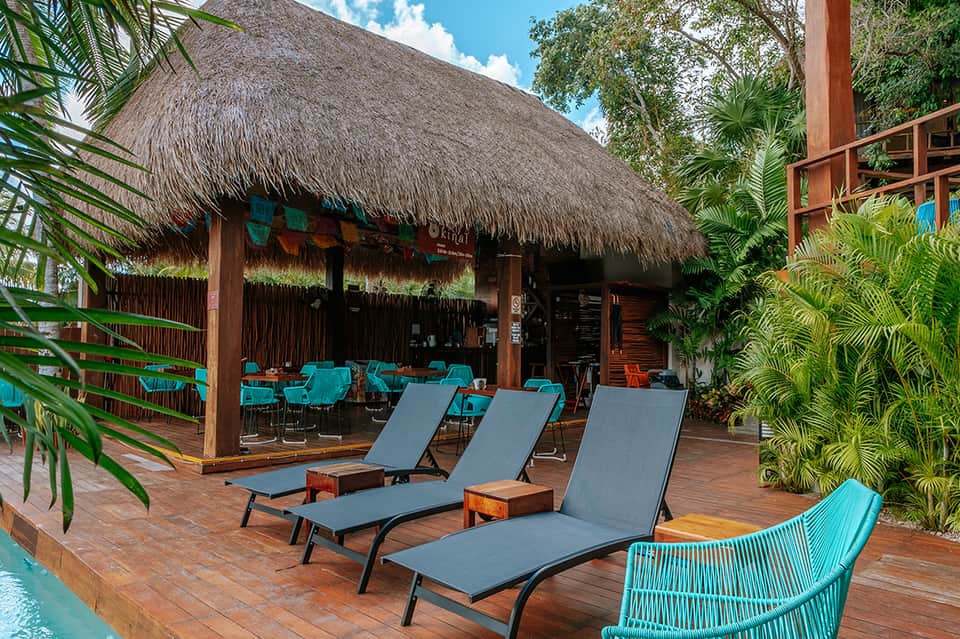 Tropical resort pool deck with thatched-roof cabana, lounge chairs, and lush palm vegetation