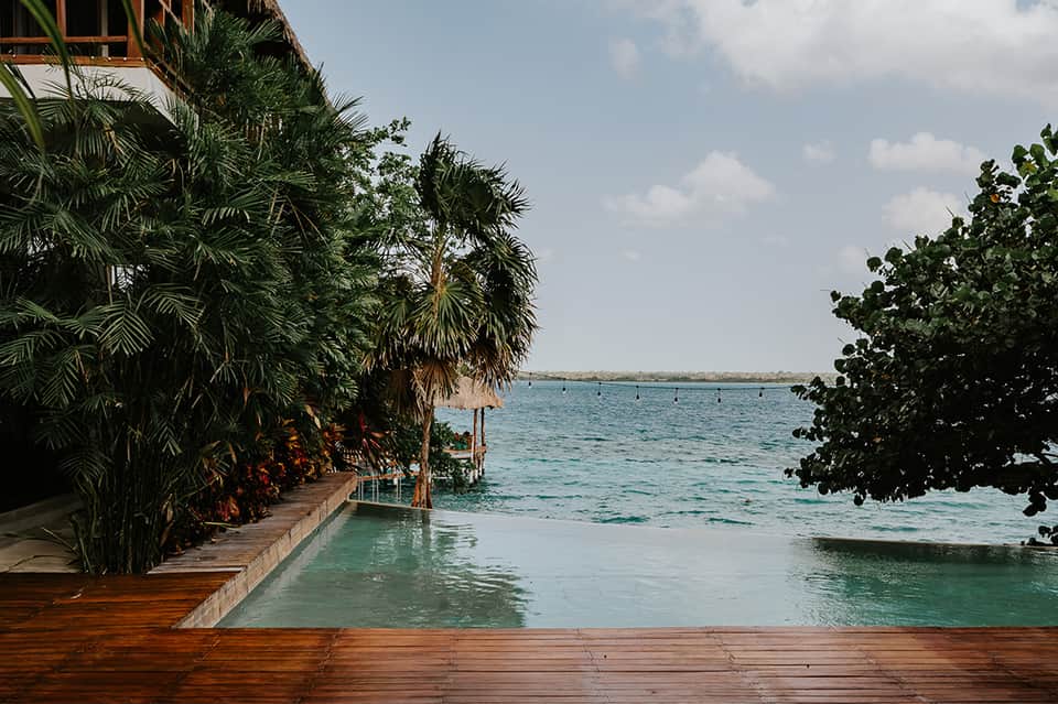 Wooden deck extending into turquoise ocean water surrounded by tropical vegetation and palm trees
