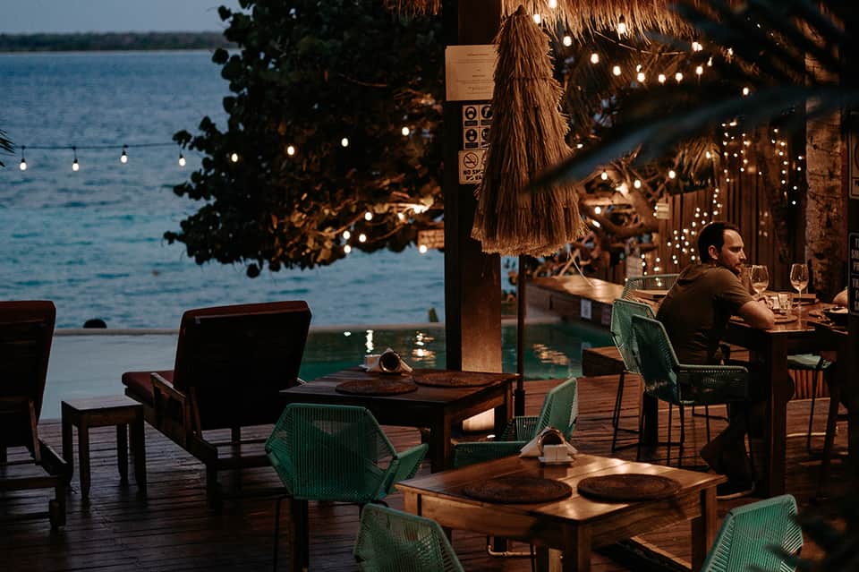 Beachfront restaurant with thatched roof, string lights, and ocean views at dusk