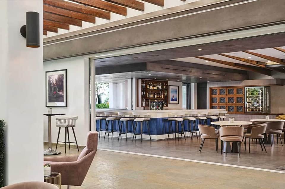 Modern resort bar and lounge with blue barstools, wooden beams, and ocean-view seating