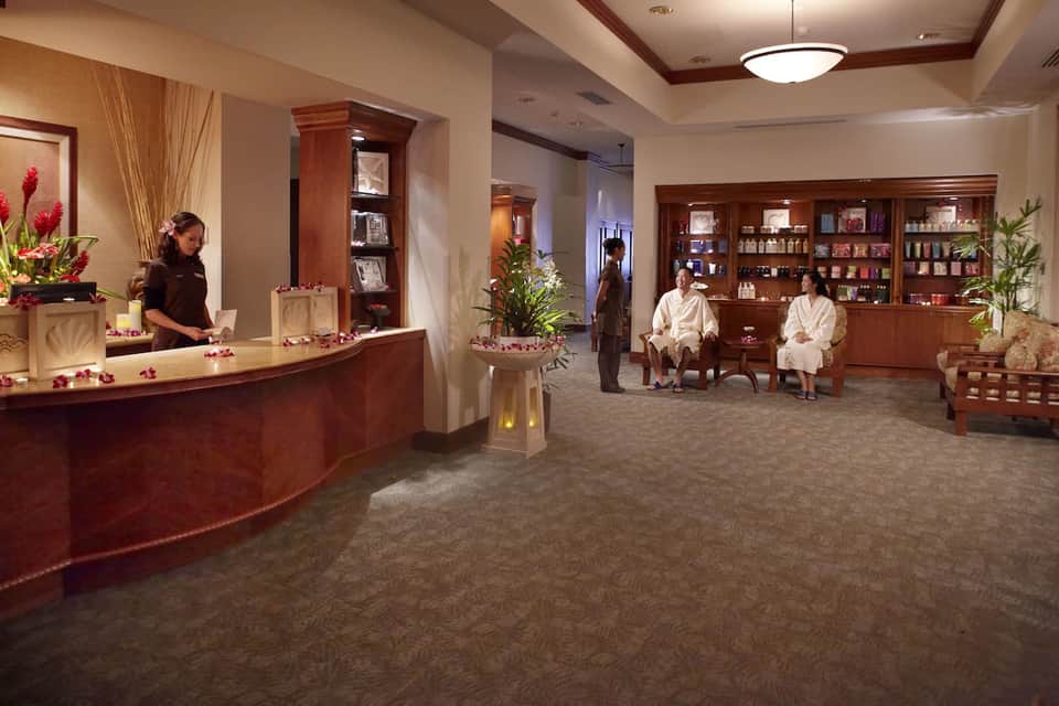 Spa reception area with wooden furnishings, tropical flowers, and relaxation seating