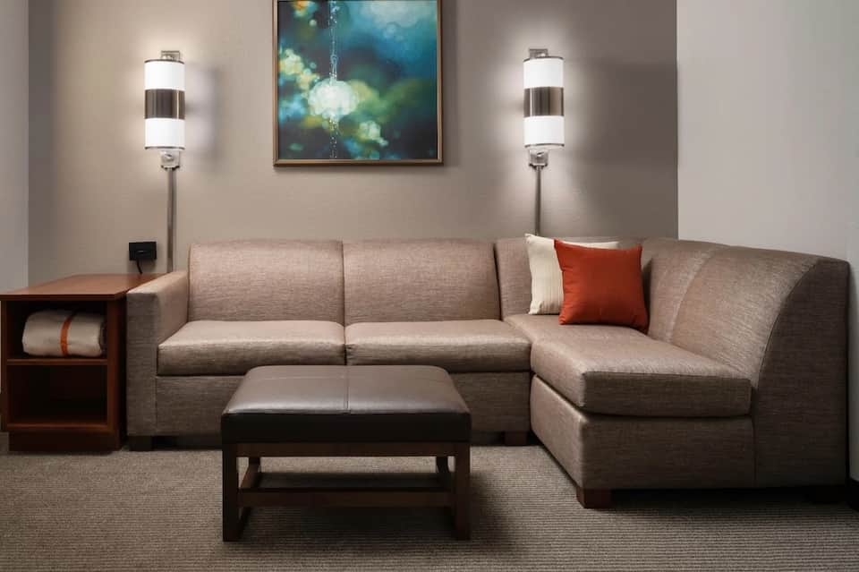 Modern hotel suite living room with sectional sofa, ottoman, and contemporary wall lighting