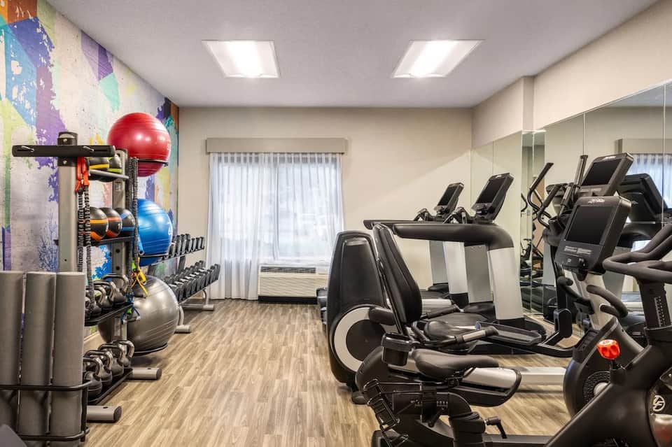 Modern fitness center with exercise equipment, colorful accent wall art, and mirrored walls