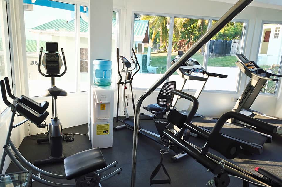 Bright fitness room with treadmills, exercise bikes, water cooler, and glass doors to outdoor patio