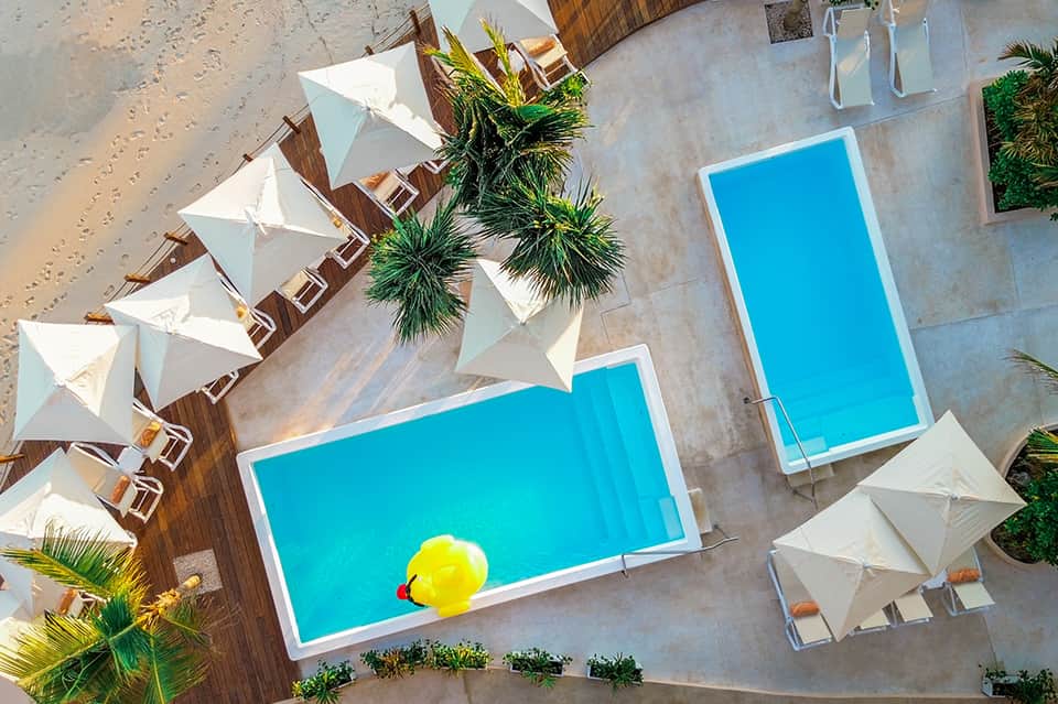 Aerial view of multiple resort pools with white umbrellas and tropical landscaping