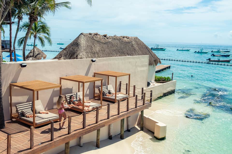 Overwater beach cabanas with lounge seating overlooking tropical turquoise ocean