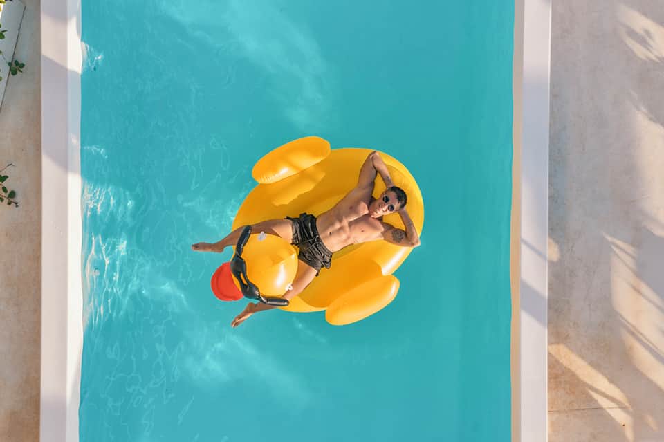 Man relaxing on yellow inflatable float in bright turquoise swimming pool