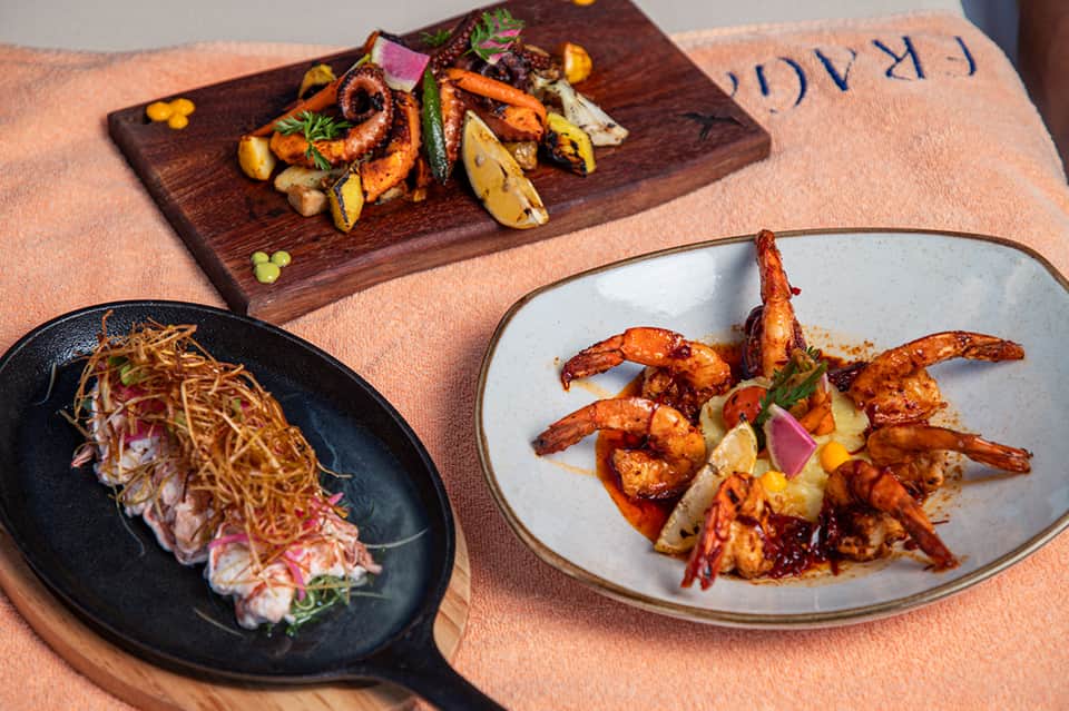 Fine dining plated seafood dishes including shrimp and octopus on wooden board and ceramic plates