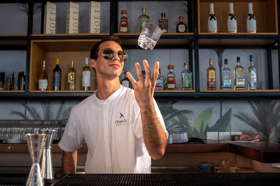 Bartender juggling glass at resort bar with bottles and tropical plants