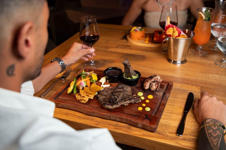Fine dining restaurant table with grilled steak, wine, and cocktails served on wooden board
