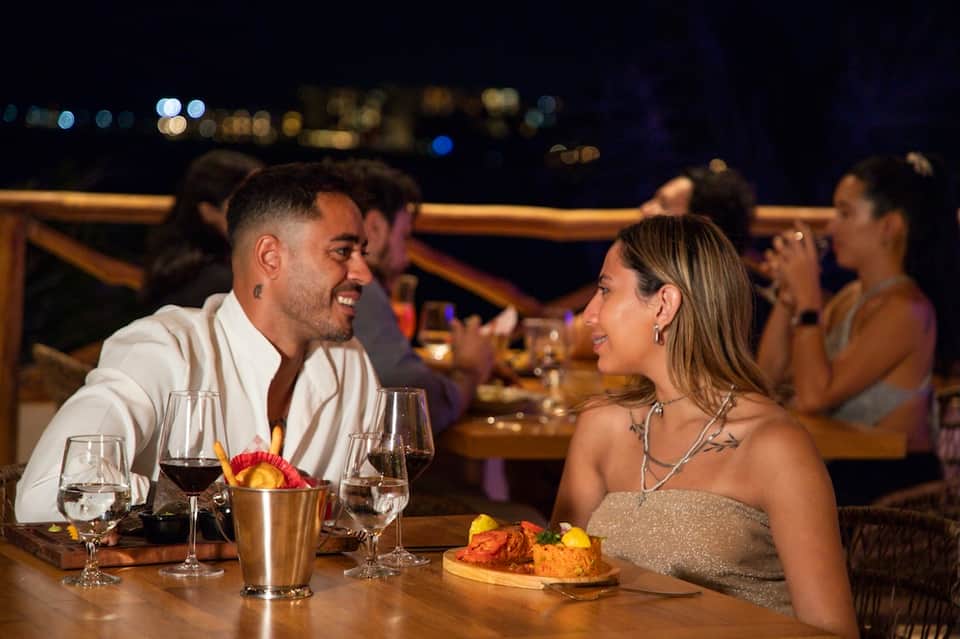Couple dining at night overlooking city lights with wine glasses, appetizers, and ambient outdoor lighting