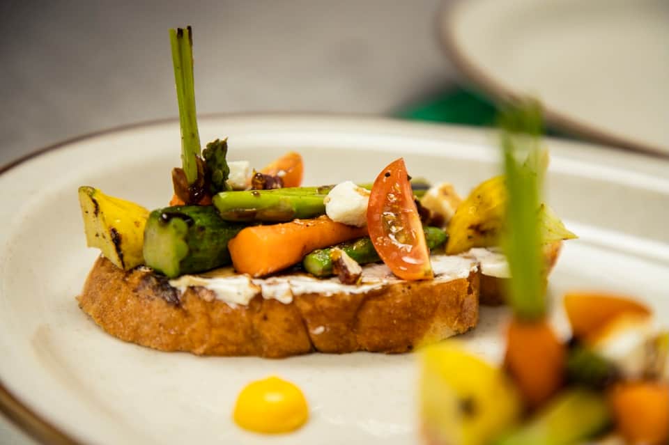 Gourmet appetizer plate with grilled vegetables, goat cheese, and asparagus spear on toasted bread