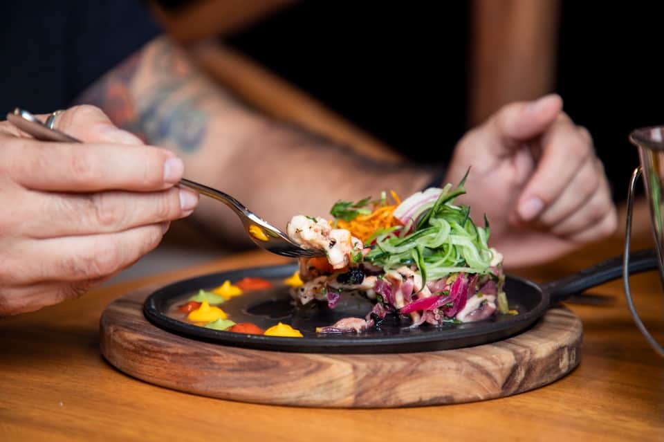 Close-up of plated seafood dish with purple cabbage and microgreens on dark plate