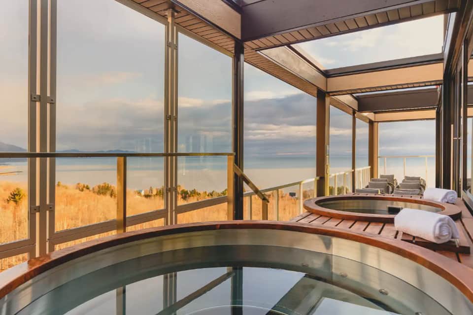 Spa room with hot tubs, floor-to-ceiling windows overlooking oceanside landscape at dusk