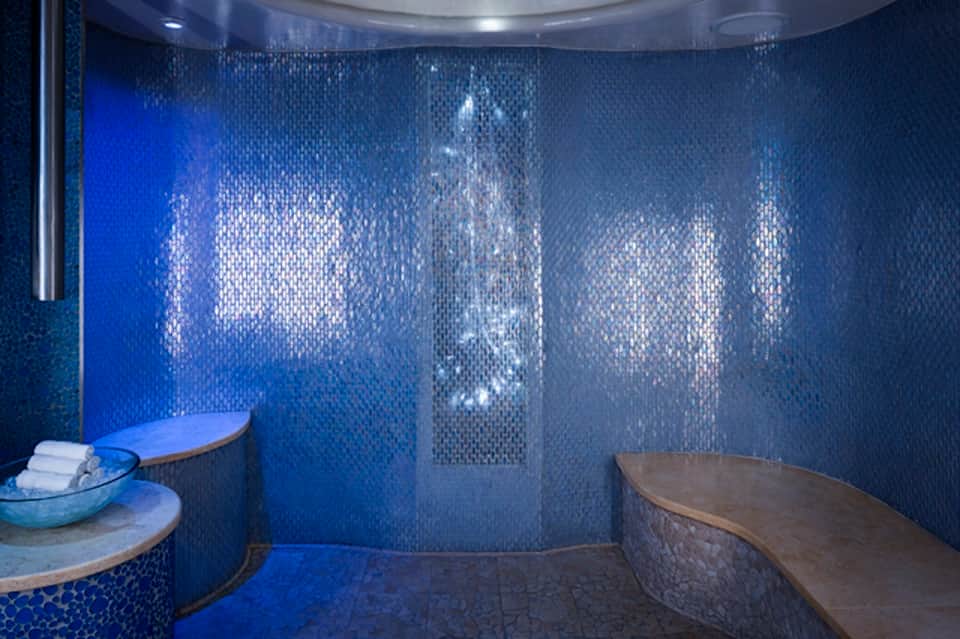 Luxury spa steam room with blue mosaic tile walls, bench seating, and atmospheric lighting
