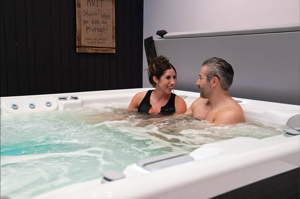 Couple relaxing in indoor hot tub with instructional sign on black wall behind them