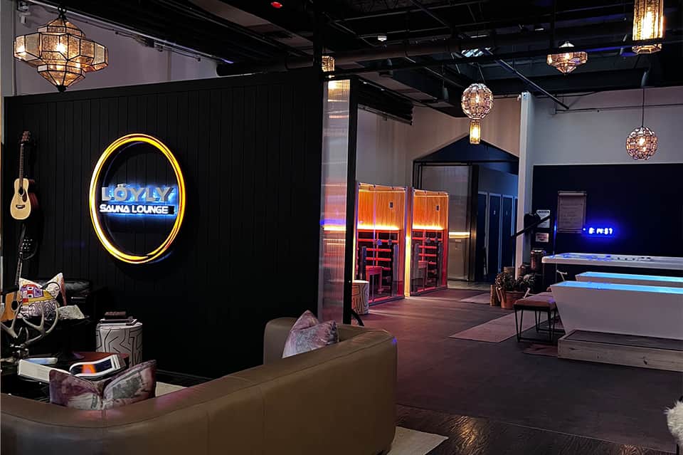 Modern entertainment venue with neon sauna lounge sign, hanging light fixtures, and bowling lanes.