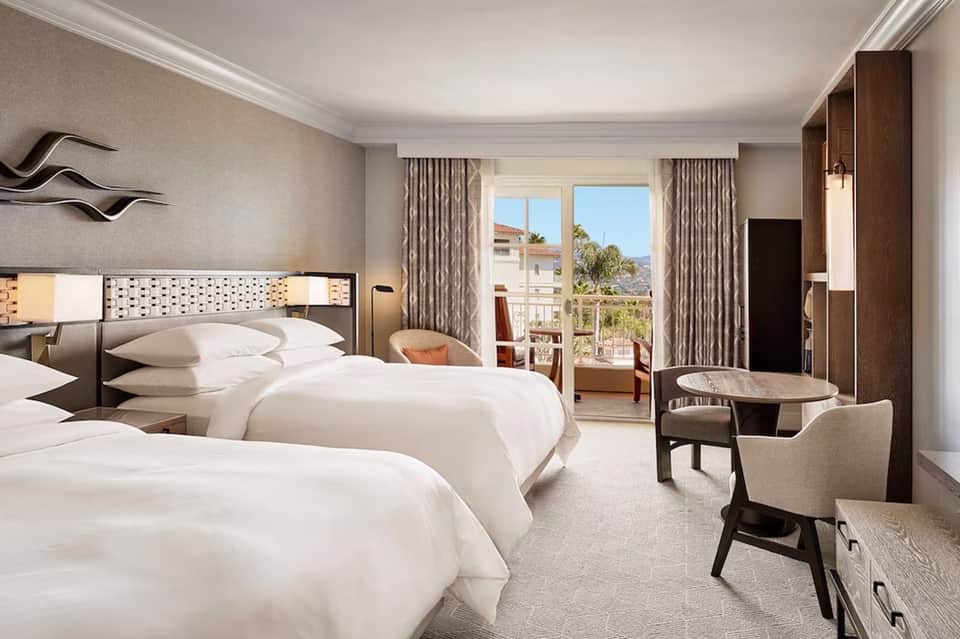 Upscale hotel room with two queen beds, balcony view, and contemporary furnishings