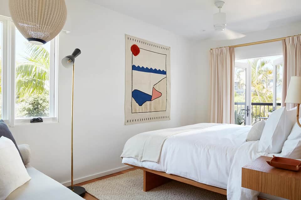 Minimalist hotel bedroom with white bedding, woven pendant light, and balcony view