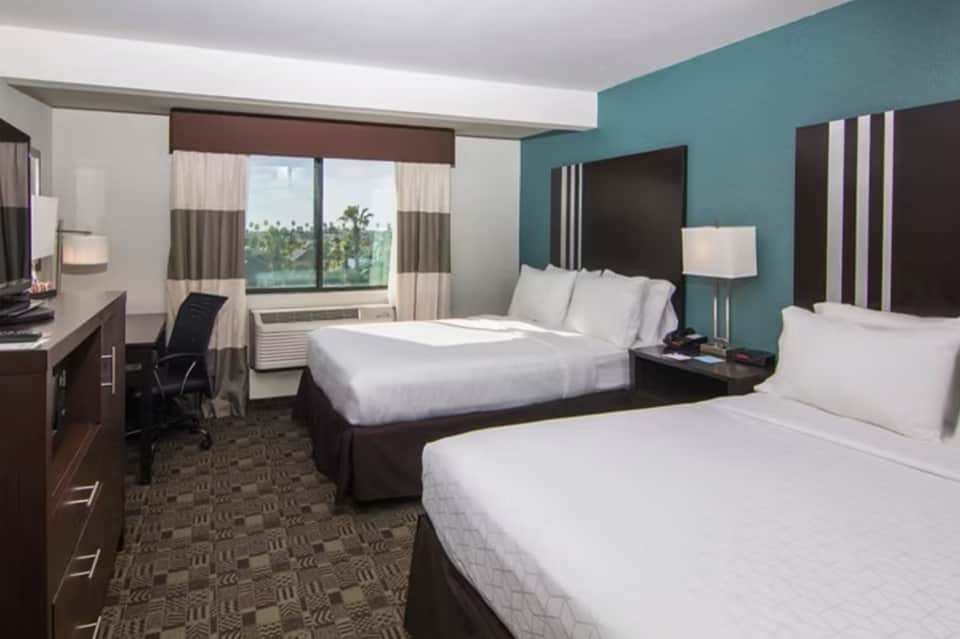 Hotel bedroom with two queen beds, teal accent wall, and ocean view windows
