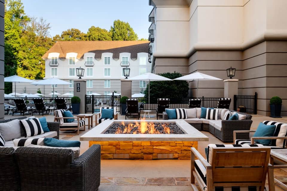 Outdoor fire pit lounge area with wicker seating, white and blue pillows, and historic building backdrop