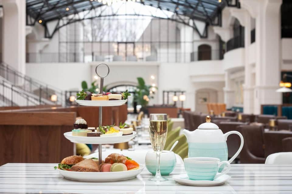 Elegant afternoon tea service in grand hotel atrium with tiered stand and champagne glasses
