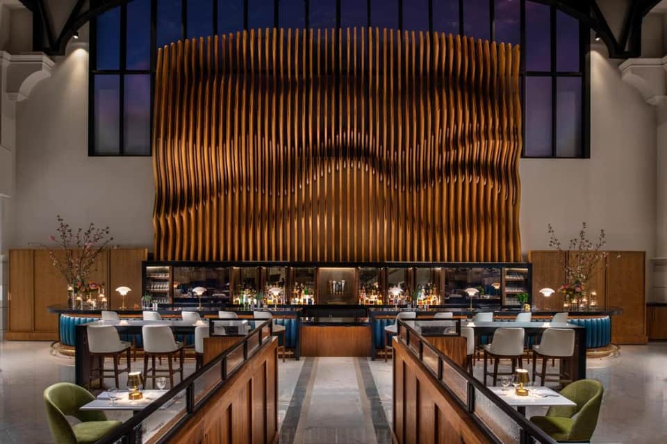 Modern hotel bar with sculptural wood feature wall, pendant lighting, and elegant seating