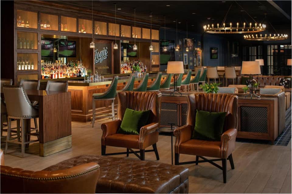 Upscale lounge bar with leather seating, wood accents, chandelier, and fully stocked shelves behind counter