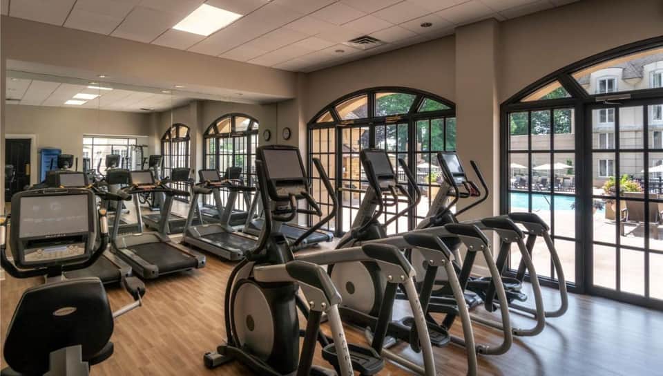 Modern fitness center with treadmills, ellipticals, and large windows overlooking pool area