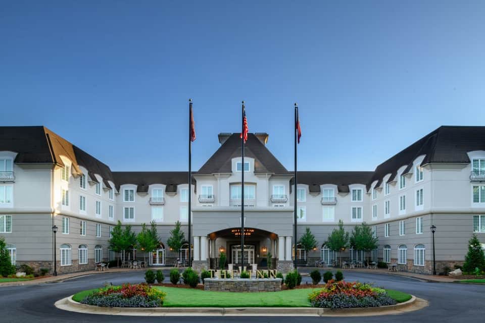 Elegant white hotel entrance with mansard roof, flags, and manicured landscaping