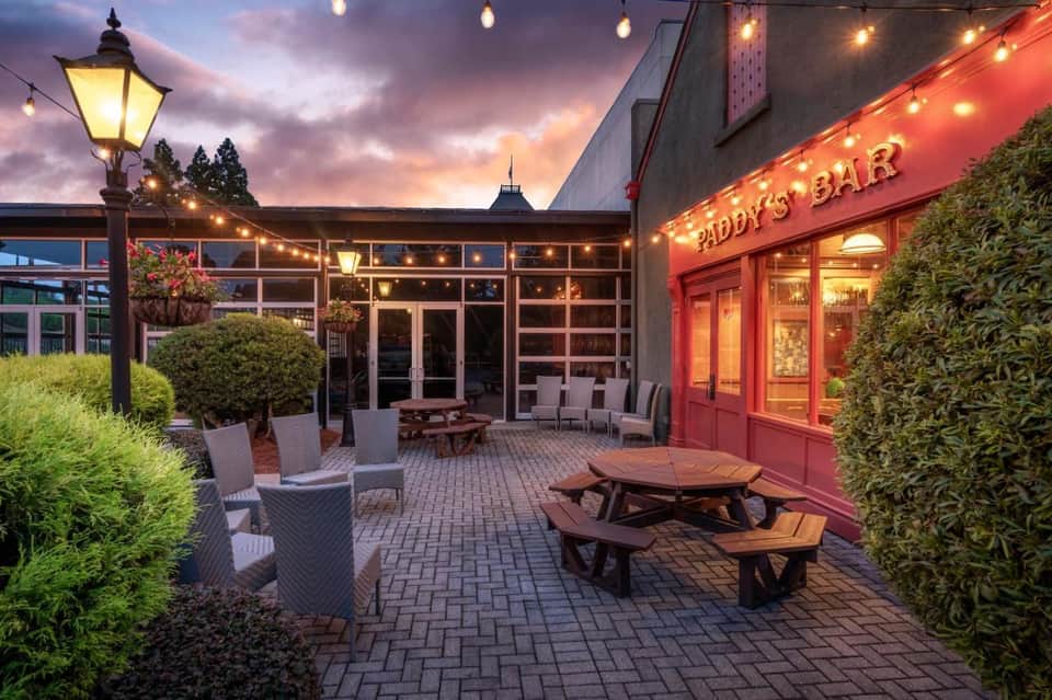Outdoor patio at dusk with Paddy's Bar entrance, picnic tables, and ambient lighting