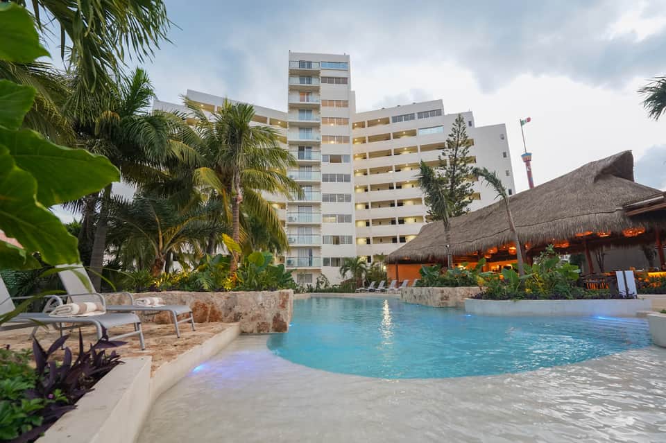 Resort pool with tropical landscaping, palm trees, and modern multi-story hotel building