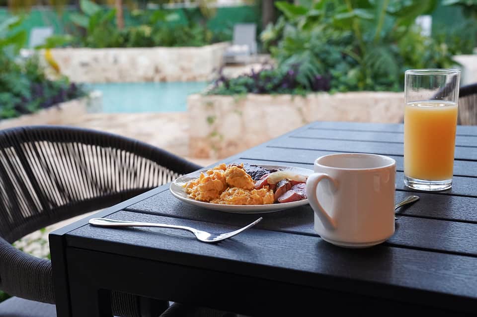 Breakfast table by pool with coffee, juice, food plate, and lounge chair