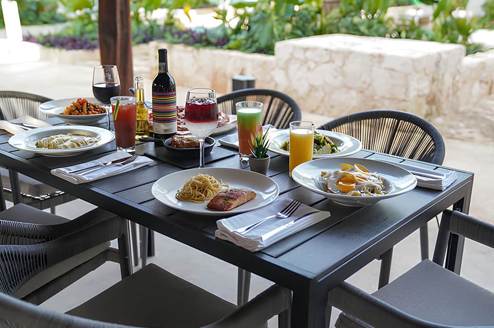 Outdoor dining table with gourmet meal, wine, and fresh juices in a landscaped garden setting