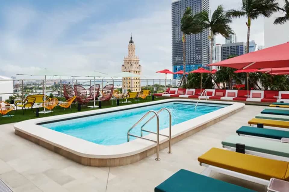 Rooftop pool with red umbrellas, yellow loungers, city skyline and historic tower views