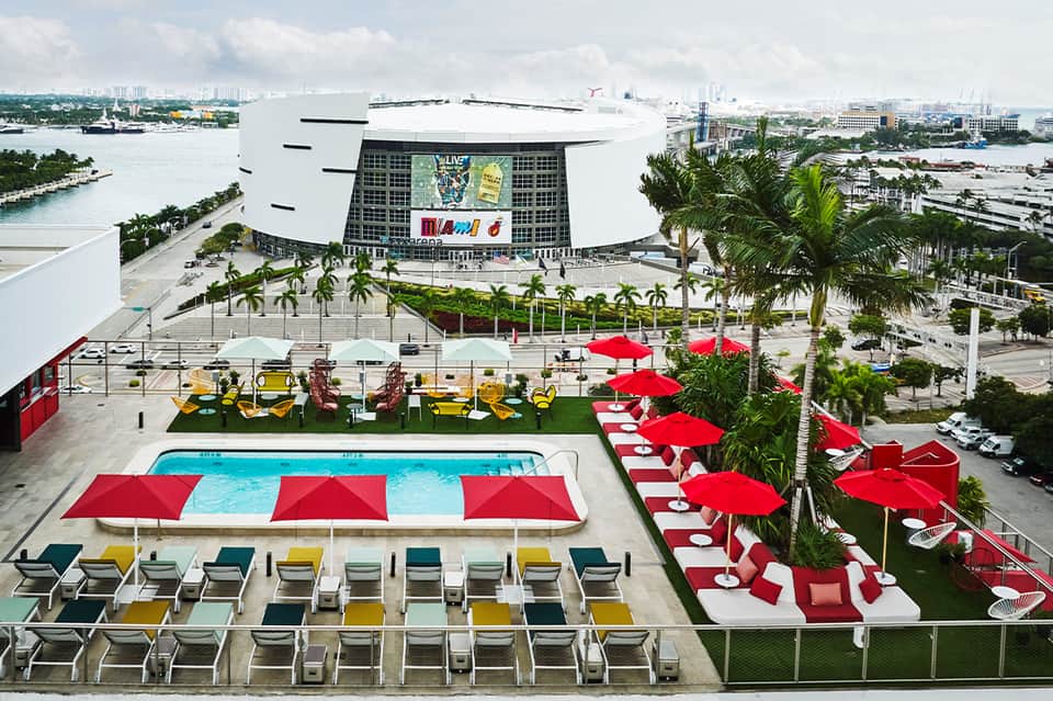 Rooftop pool with red umbrellas overlooking Miami arena and waterfront cityscape