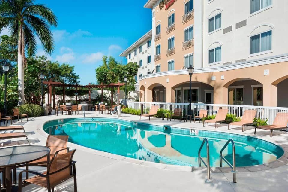 Resort outdoor pool with turquoise water, lounge chairs, peach building facade, and palm tree landscaping