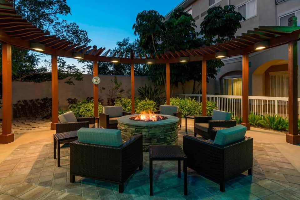 Outdoor patio with fire pit, lounge seating, wooden pergola, and accent lighting at night