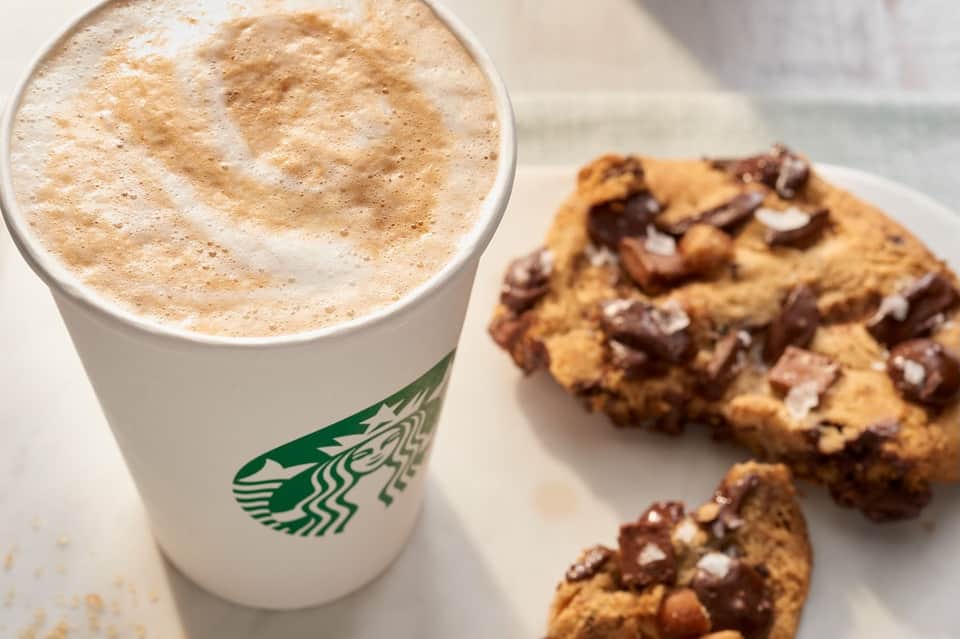Starbucks coffee drink with chocolate chip cookie on white plate by window