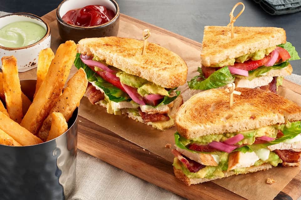 Gourmet sandwiches with crispy fries and avocado spread on wooden serving board