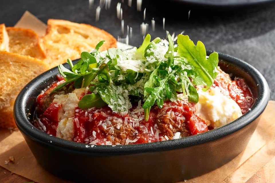 Gourmet pasta dish in black skillet topped with fresh herbs and parmesan, accompanied by bread on wooden surface