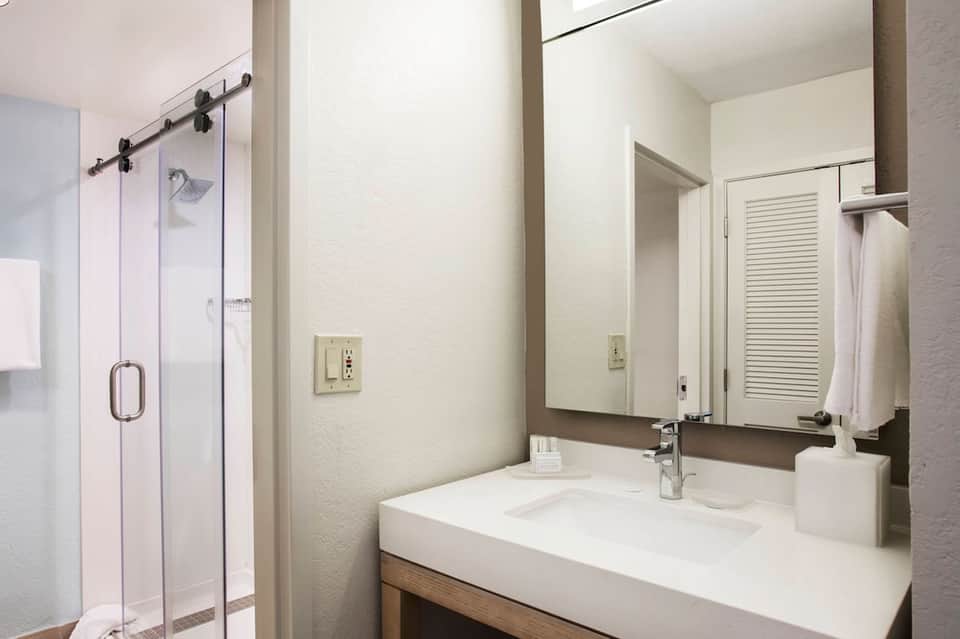 Modern hotel bathroom with white vanity, large mirror, and walk-in glass shower enclosure