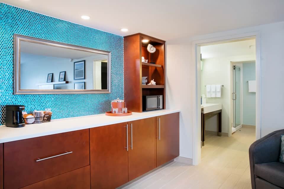 Modern bathroom vanity with turquoise mosaic tile backsplash, large mirror, wooden cabinetry, and spa access