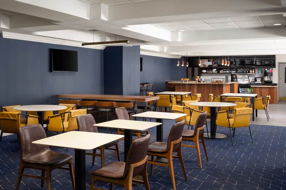 Contemporary café with navy accent walls, yellow chairs, wooden tables, and coffee bar