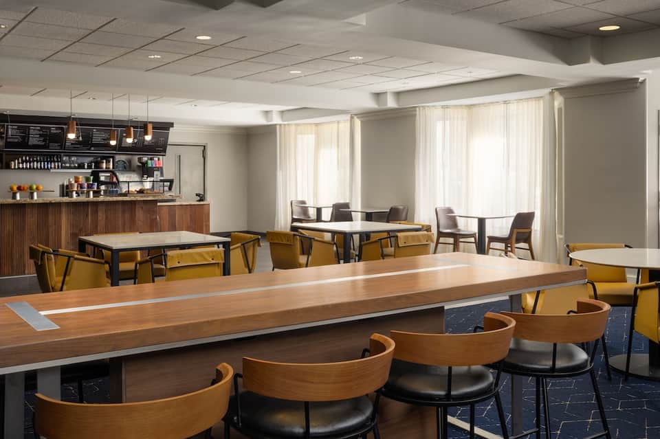 Modern hotel dining area with wood tables, yellow chairs, and coffee bar