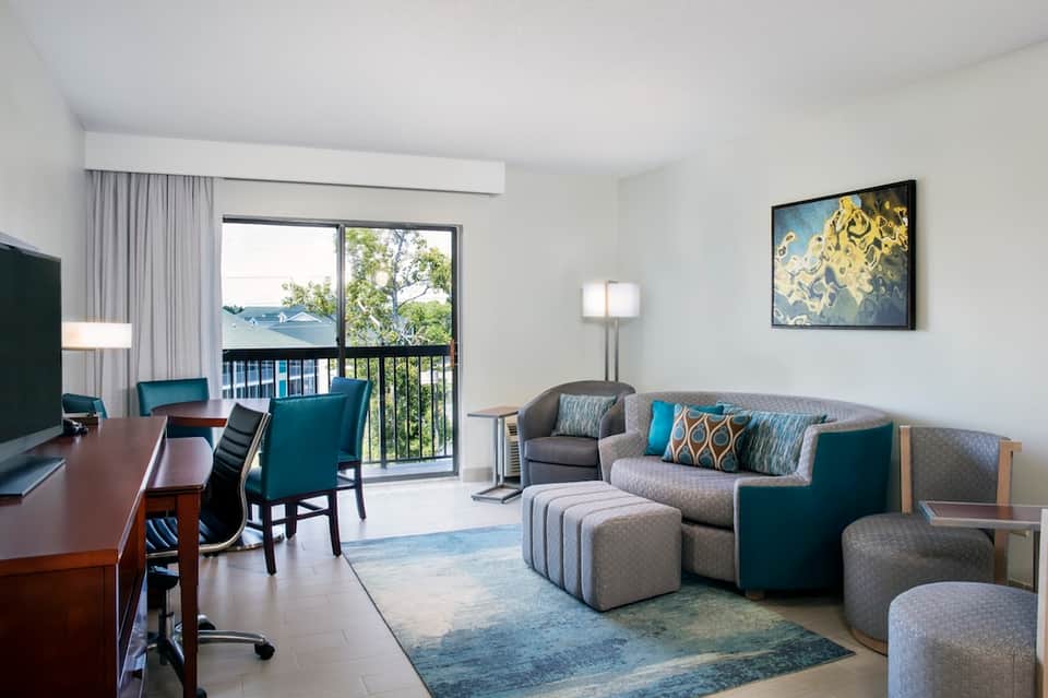 Modern hotel suite with desk, sofa, balcony view, and contemporary furnishings