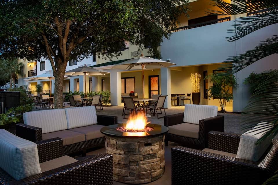 Outdoor patio area with fire pit, lounge seating, palm trees, and illuminated modern architecture