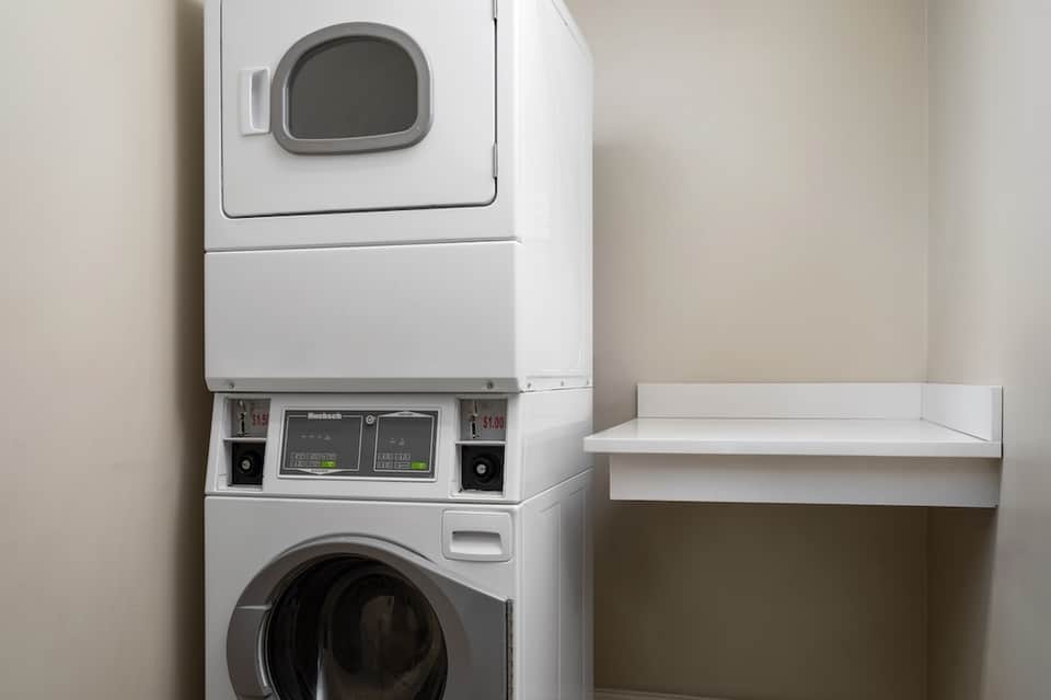 Stacked washer and dryer units in bright laundry room with white shelving
