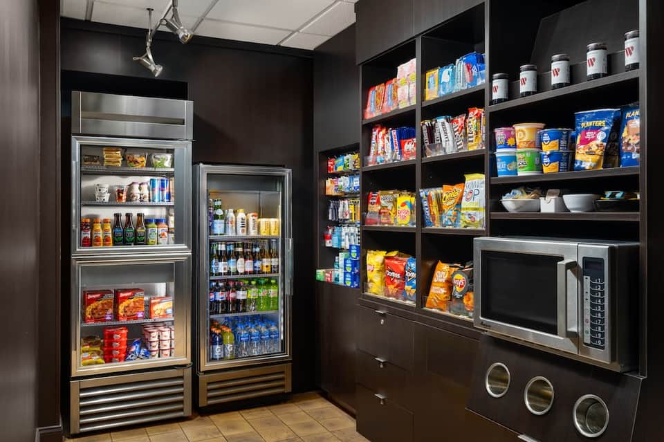 Hotel snack bar with glass-front refrigerators, shelving with beverages and snacks, and microwave