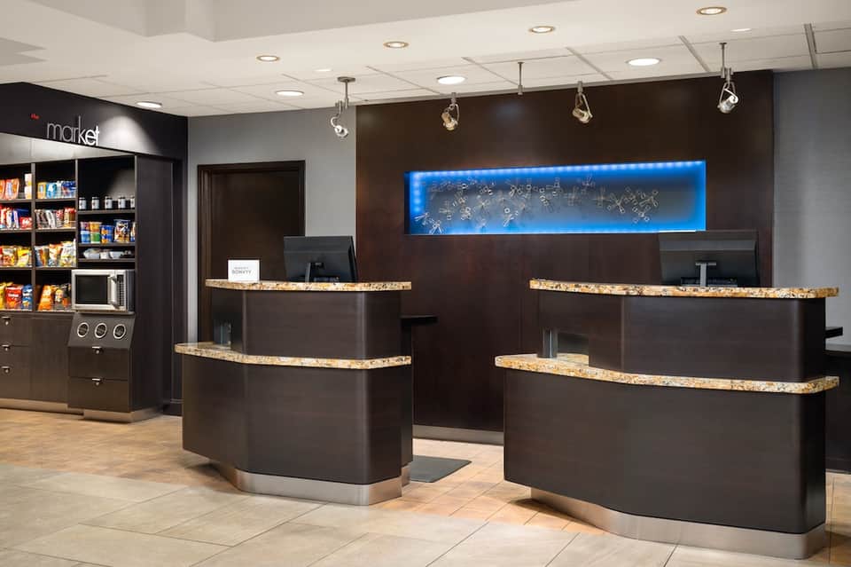 Modern hotel reception area with dark wood counters, gold accents, and market shelving